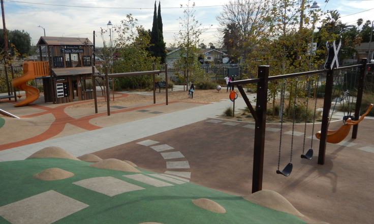 Two-level play structure, swings and trees on rubber-covered ground.