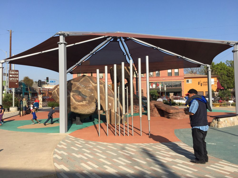 Man stands infront of a seven metal tubes near a covered play area.