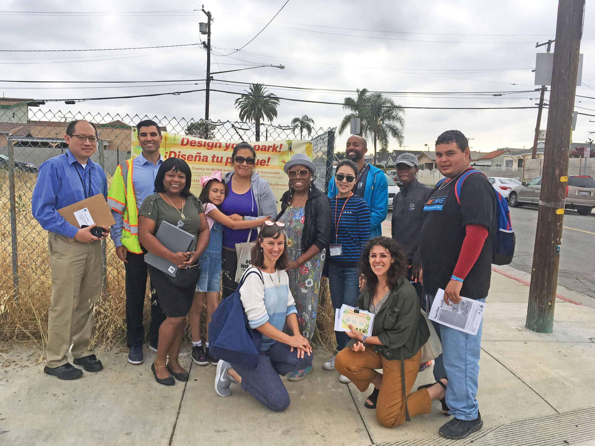 A group of people gathered outside a fenced vacant lot during a planning meeting