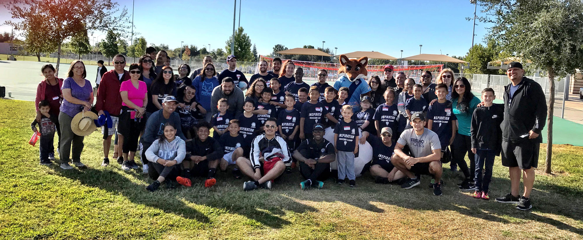 A large group of people sitting, kneeling, and standing in a grassy park posing for a photo op