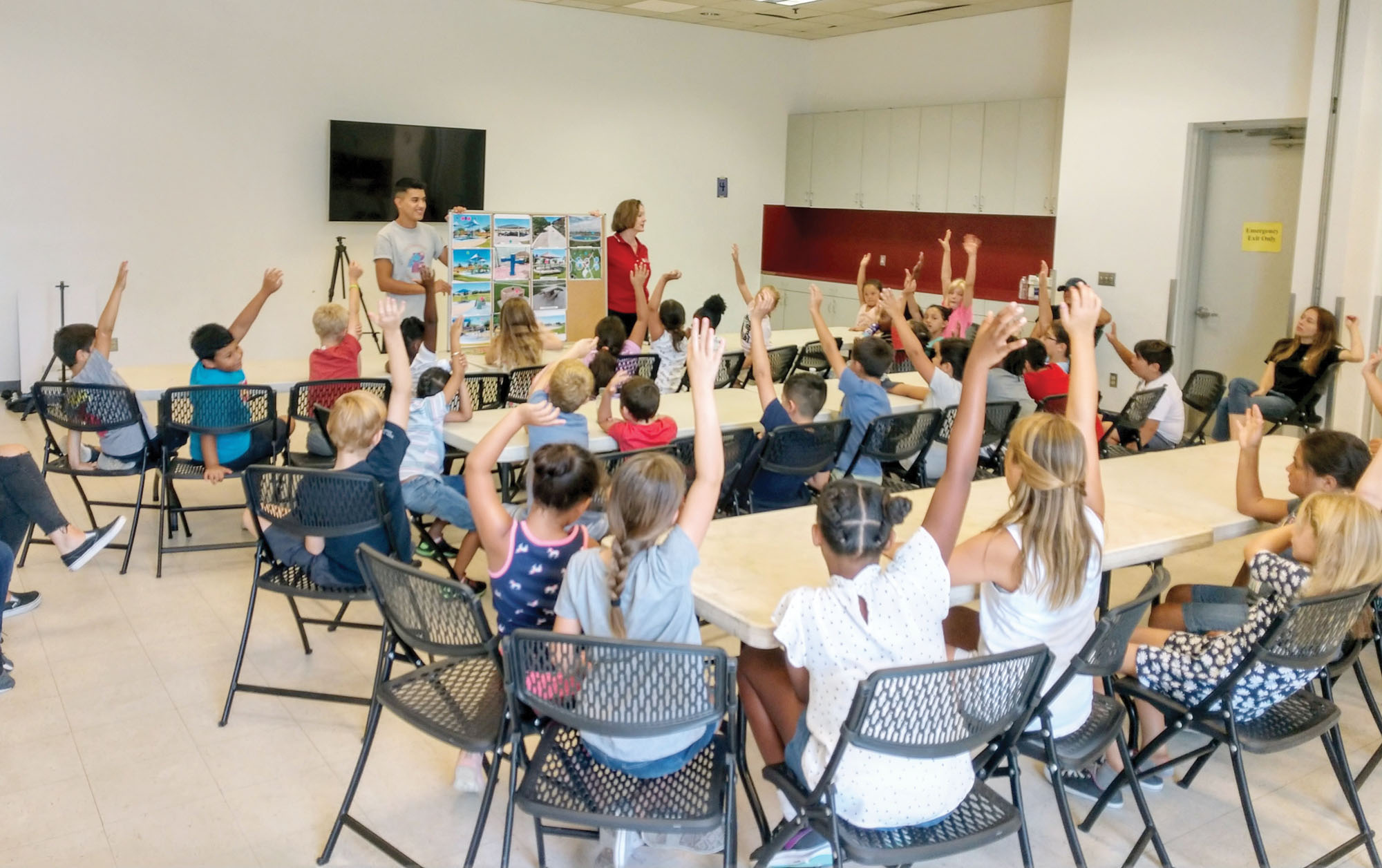 Children in a classroom, raising their hands during a park planning process meeting