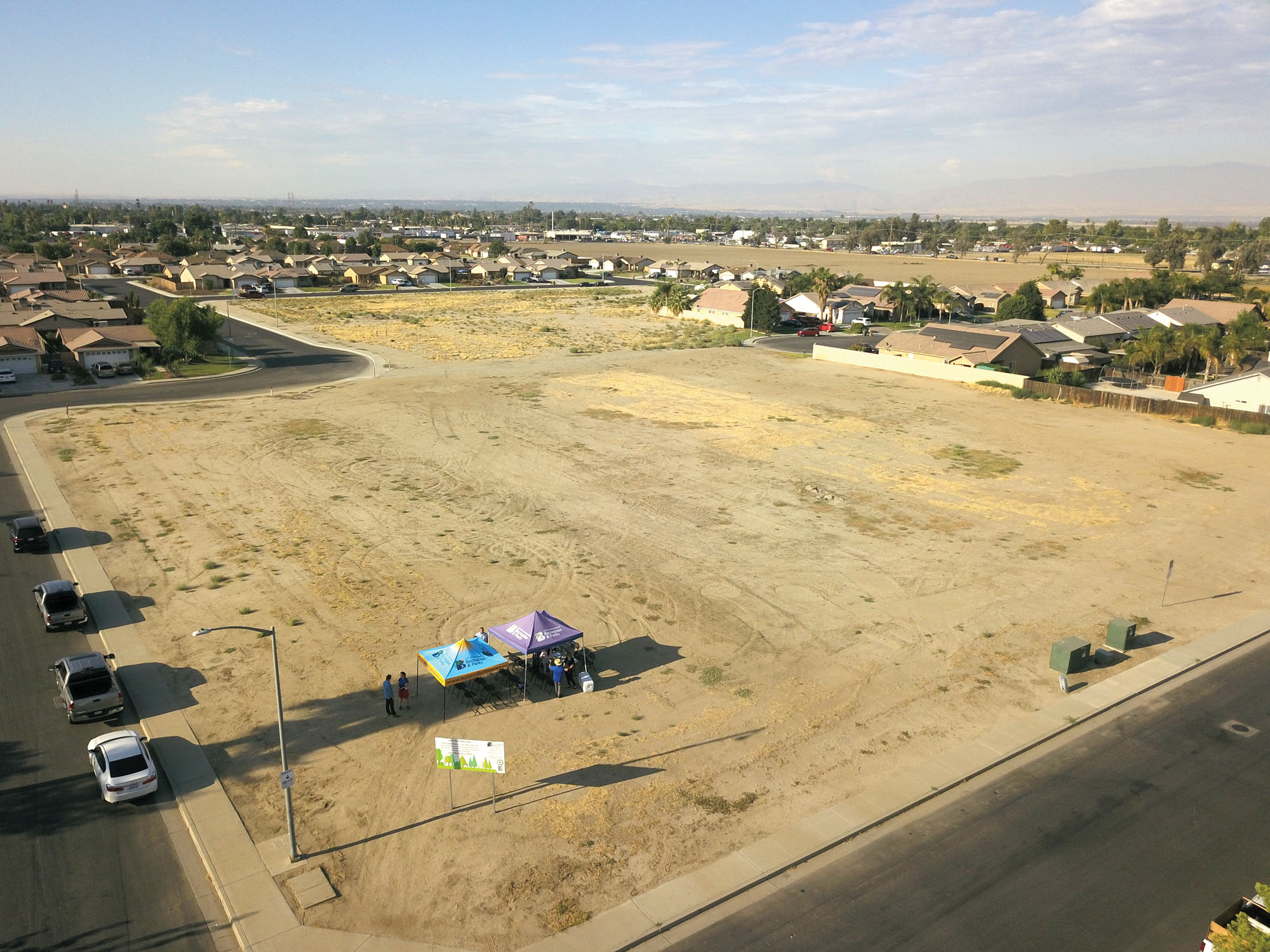 An oblique view of a vacant dirt lot with people meeting under temporary canopy tents