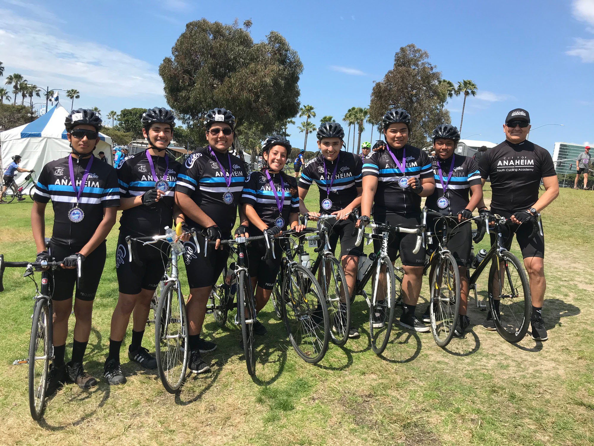 A group of adults with their bikes and matching jerseys. They have medals around their necks.