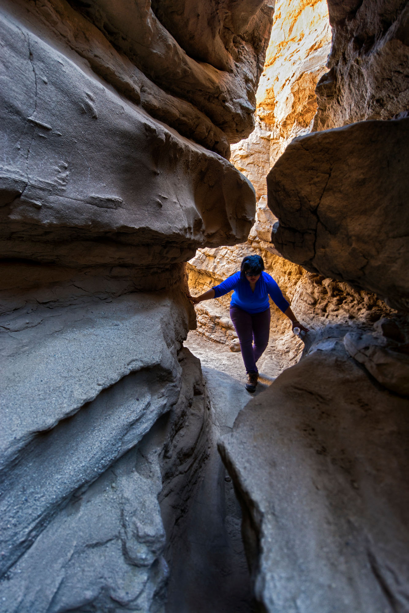 A woman hikes through a rock crevasse, with the sunlight behind her