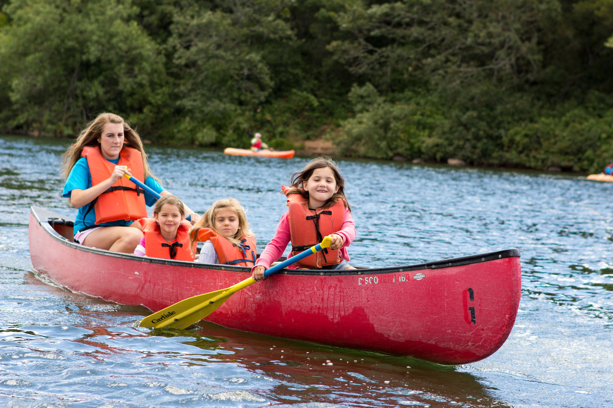 A woman and three girls paddle a red canoe on a lake