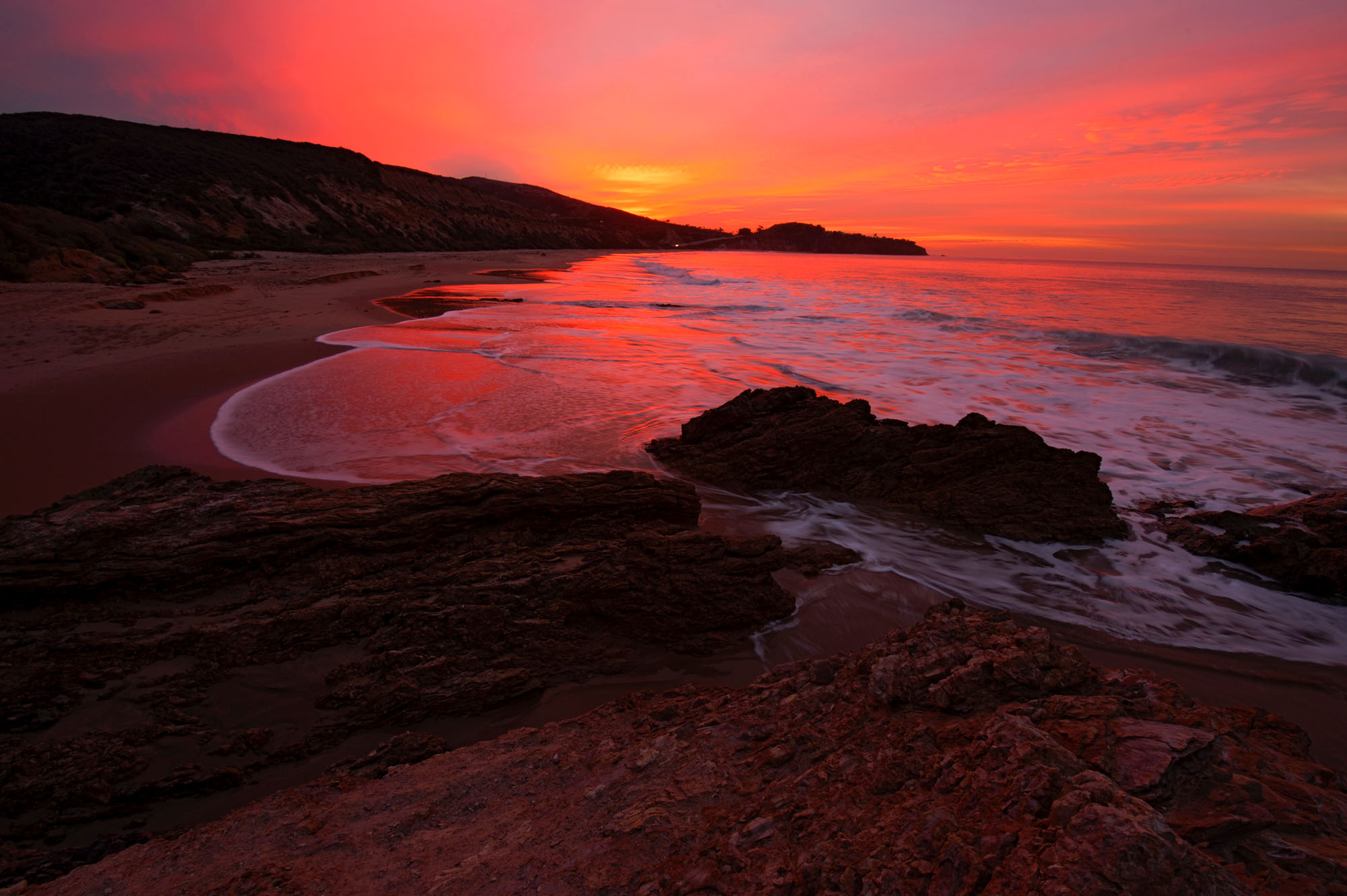 Sunset with orange and pink sky reflecting off of the waves rolling onto the beach