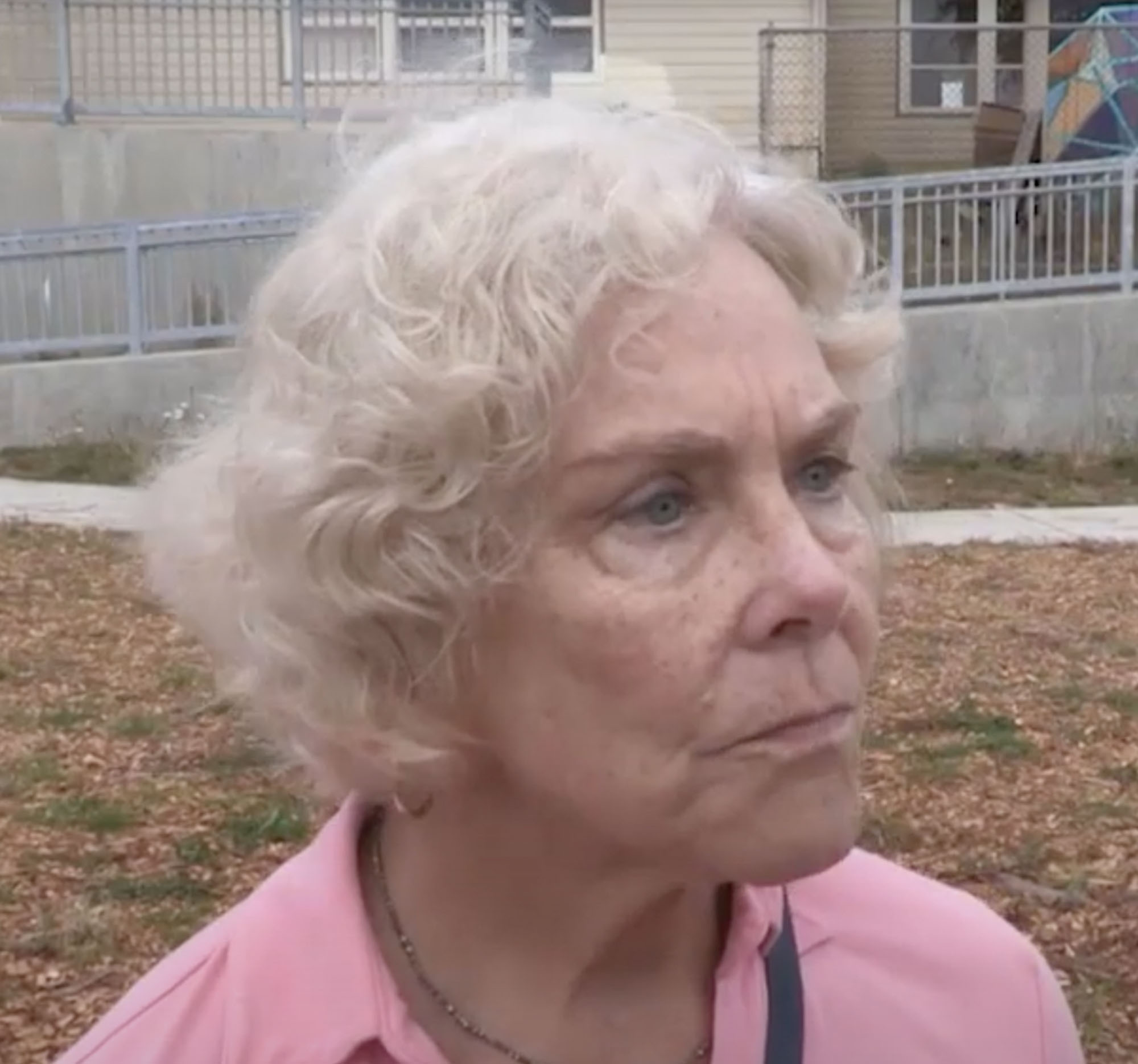 A woman wearing a pink shirt standing outside and listening to someone off camera