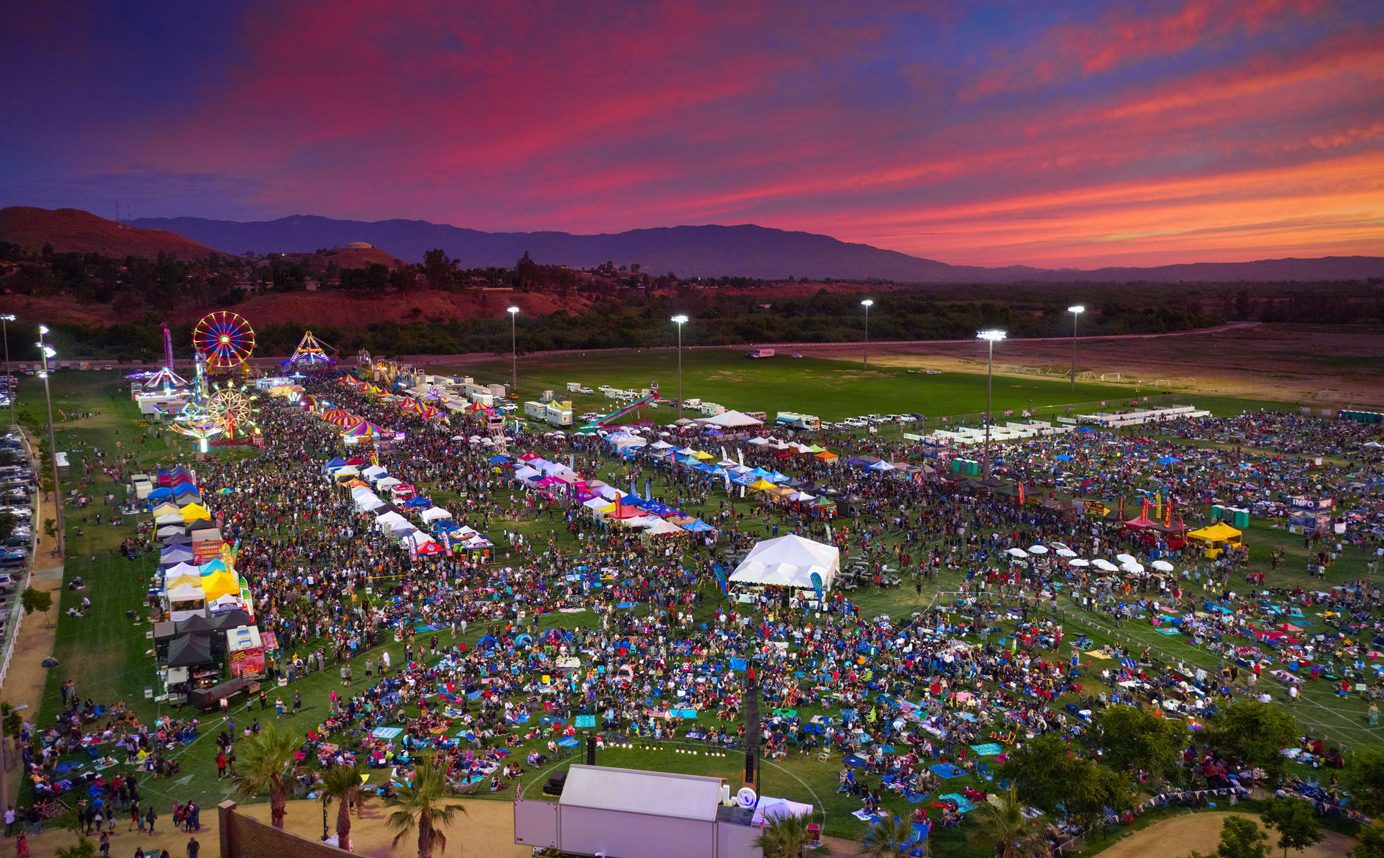 Sunset with colorful sky in an oblique aerial view of a fair with rides, vendors, and a stage