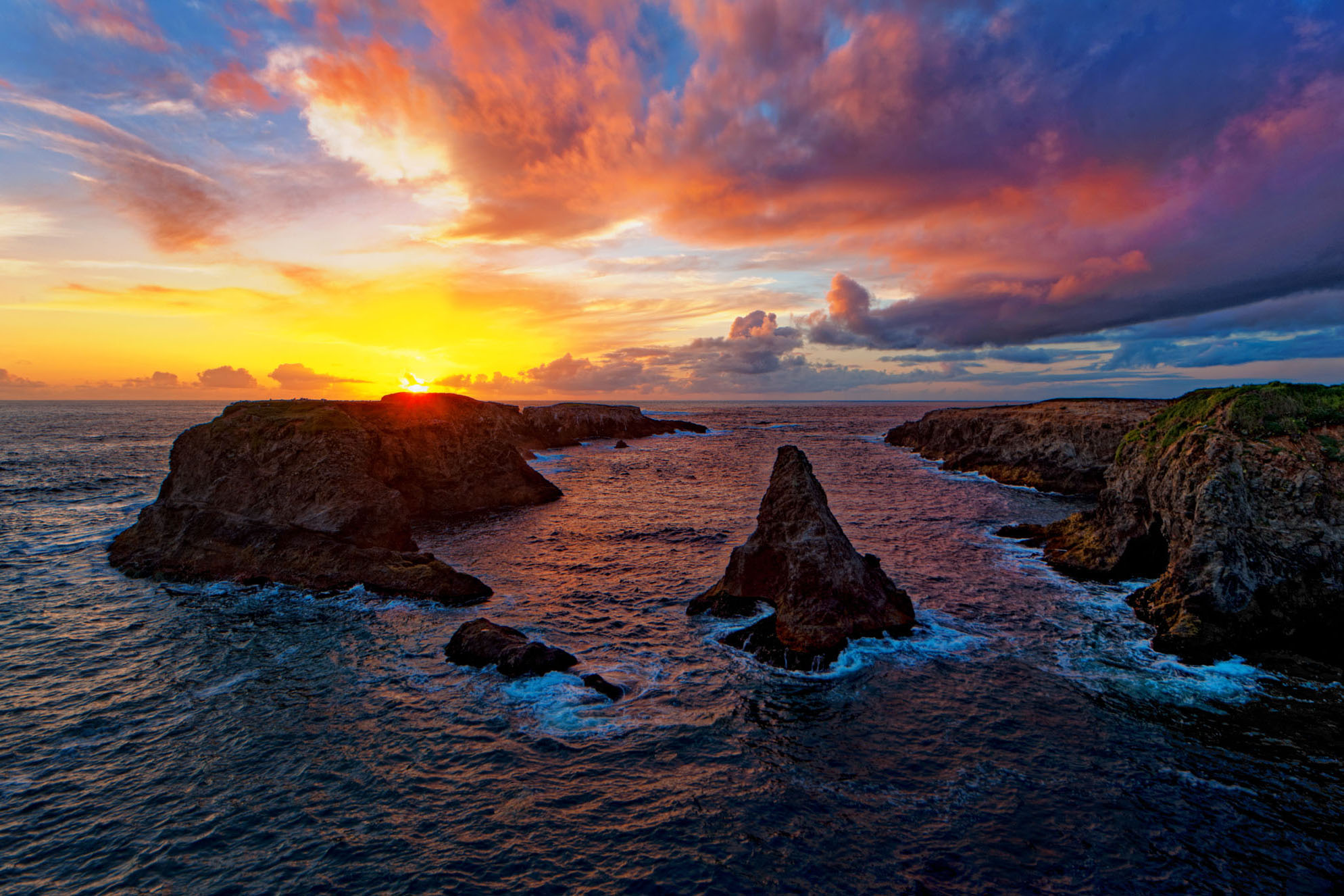 Rocky islands near the rocky shore as the sun sets with a colorful, partly cloudy sky