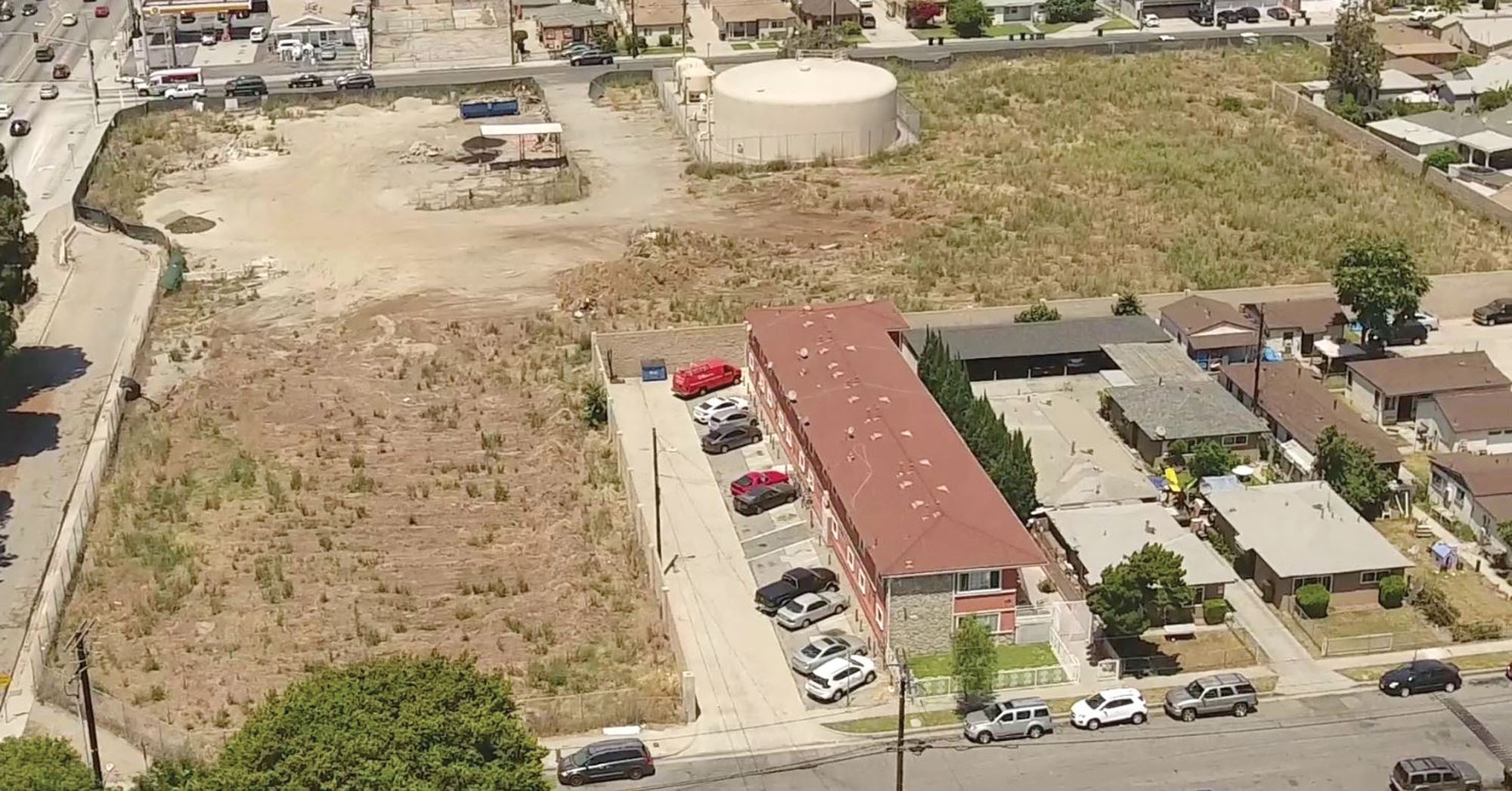 An oblique view of a vacant lot with shrubs surrounded by temporary fencing and a concrete wall