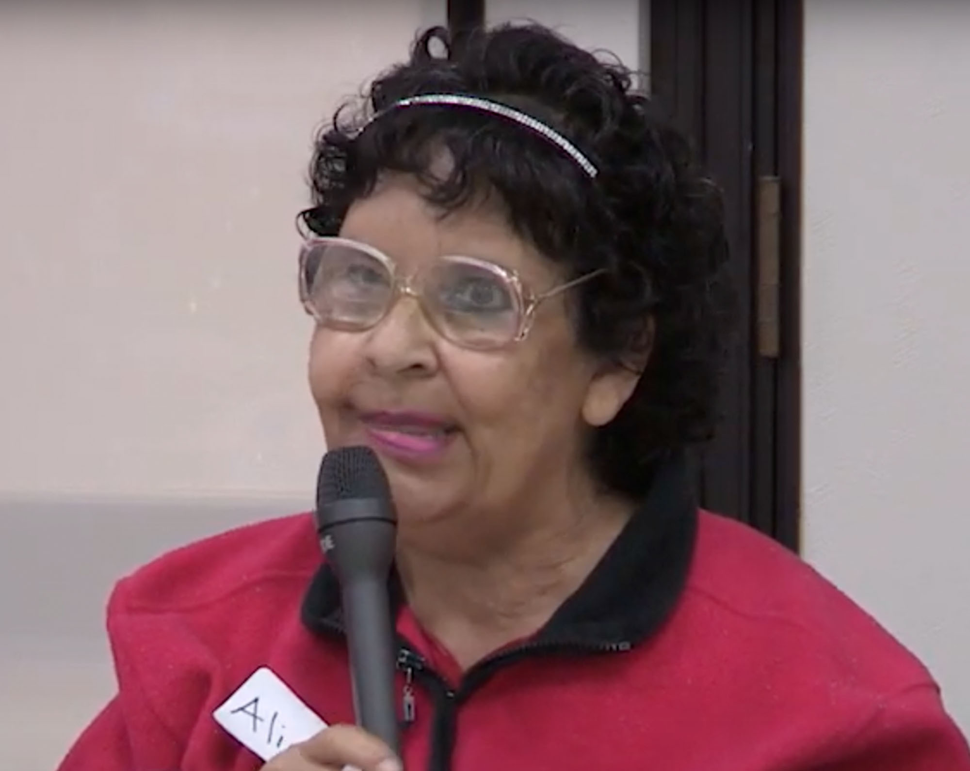 A woman with a nametag speaking into a microphone in a conference room