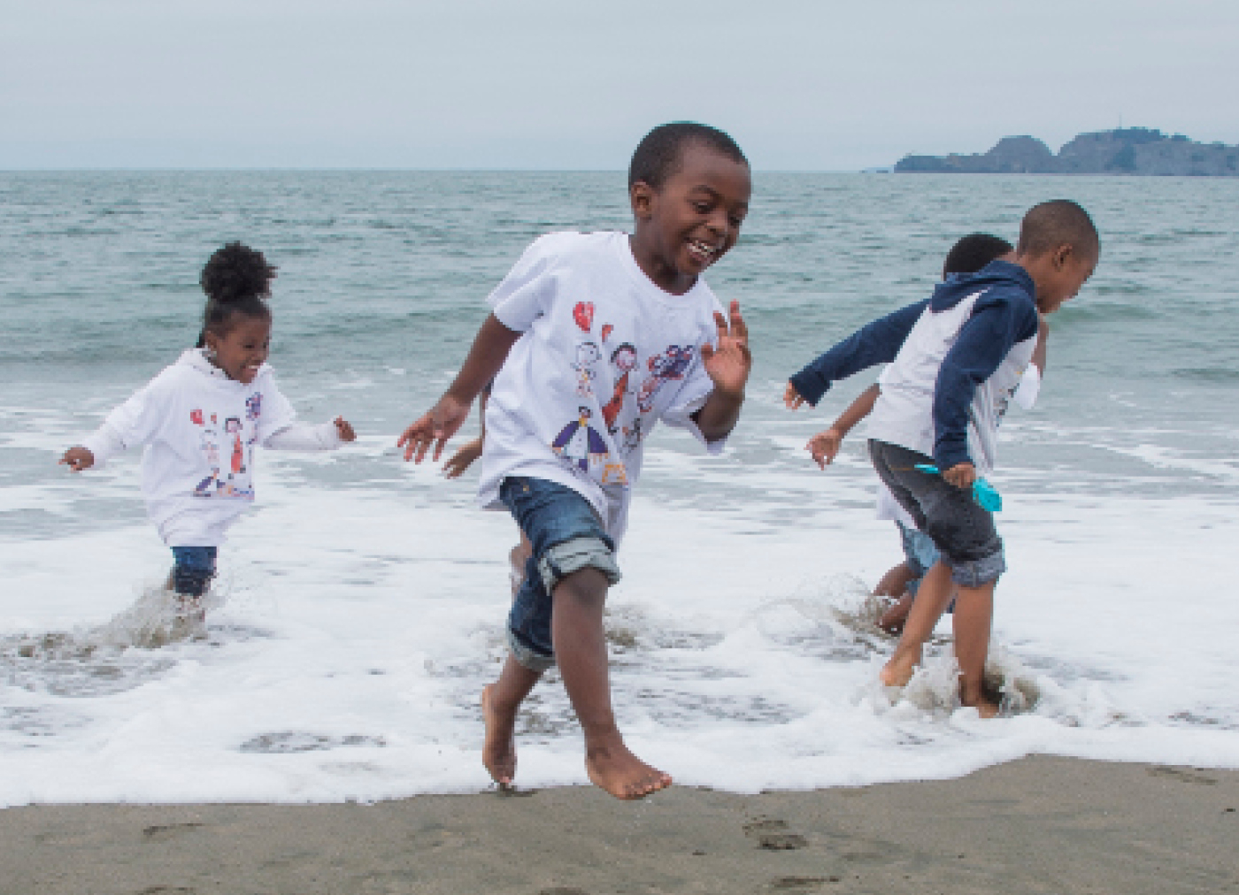 Children in shorts and t-shirts smile and splash in the small waves on the beach