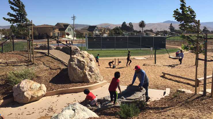 People playing in a park with boulders and a wood chip play area