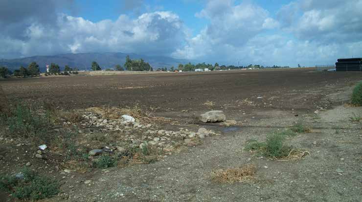 A vacant lot with dirt and some rocks with hills in the background and partly cloudy skies