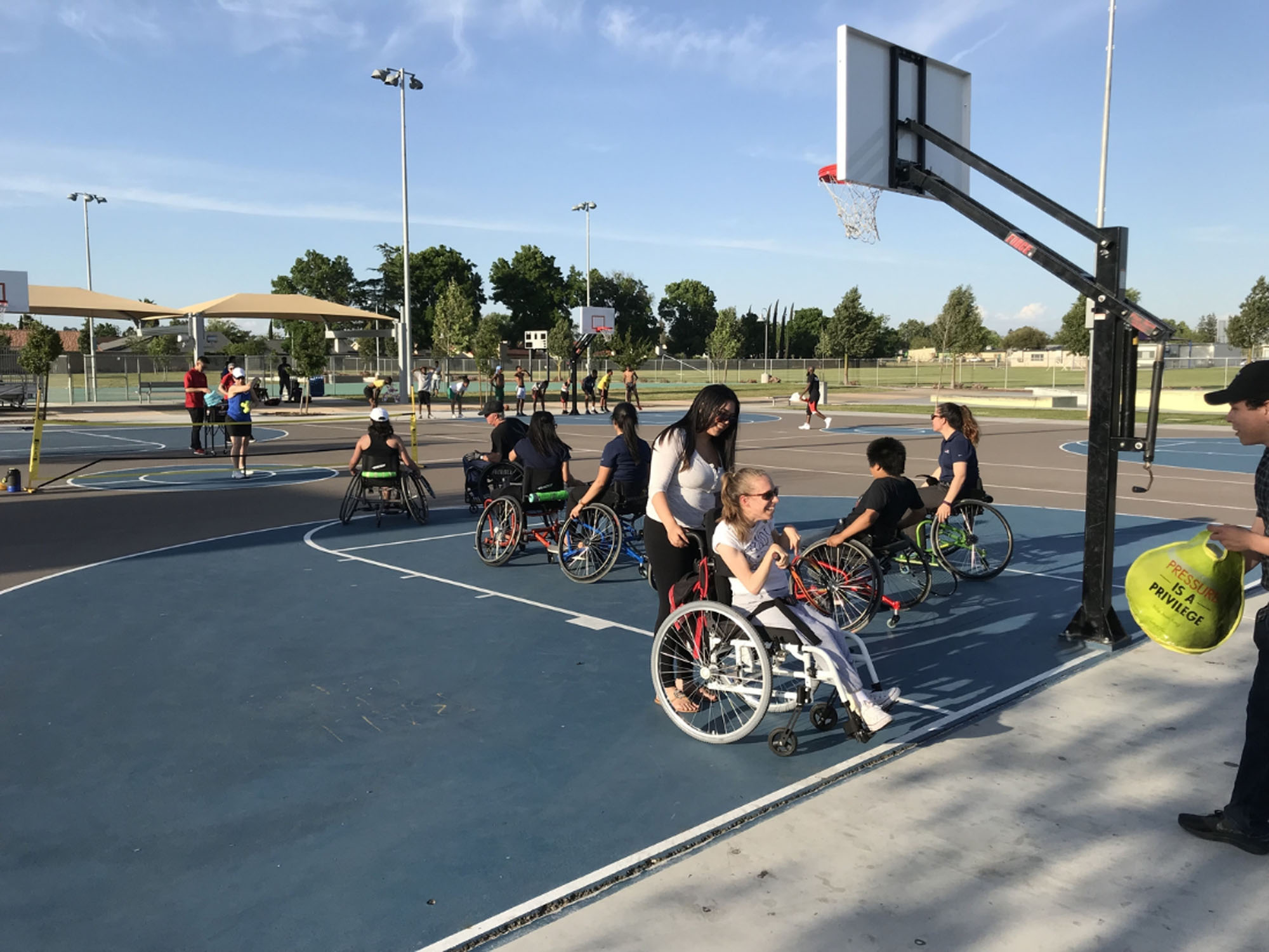 Teenagers and adults in sport wheelchairs on a basketball court at a large park
