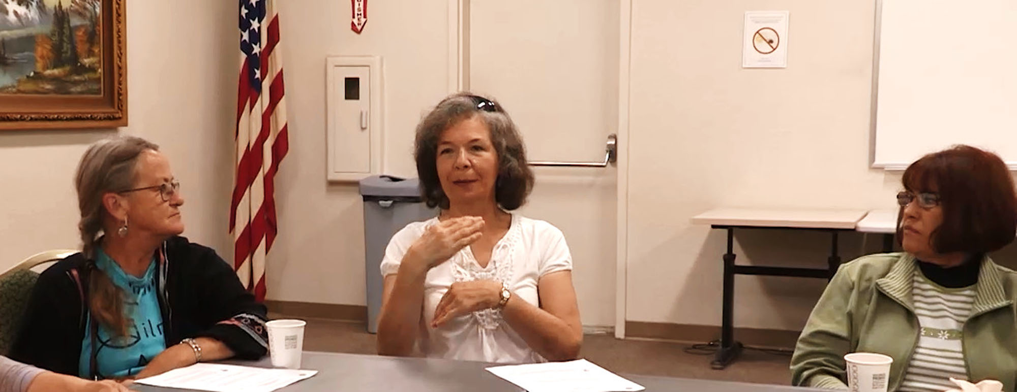 A woman speaking in a meeting in a conference room with two women on either side of her listening