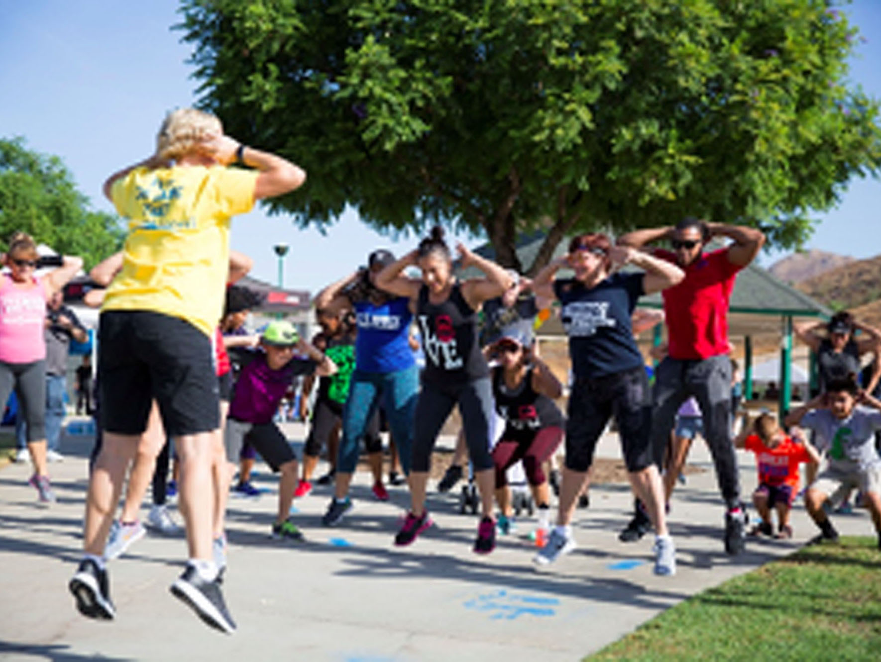 People doing jumping exercises with an instructor in front of a large tree with green leaves