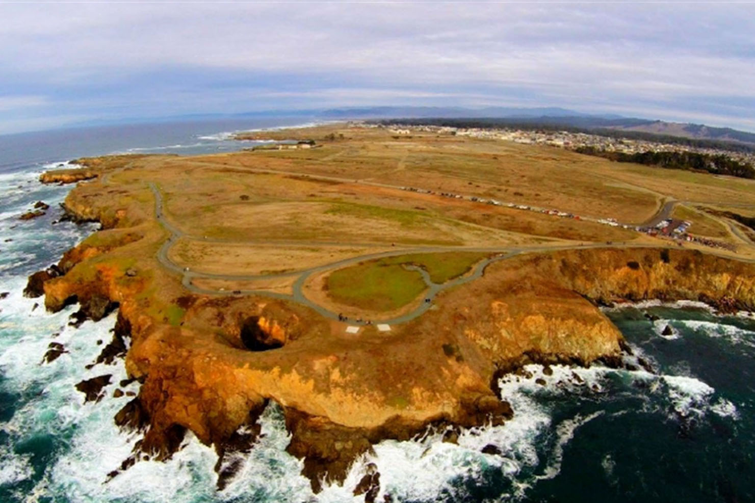 An oblique view of a rocky shoreline and below a plateau with a parking lot and wide trails