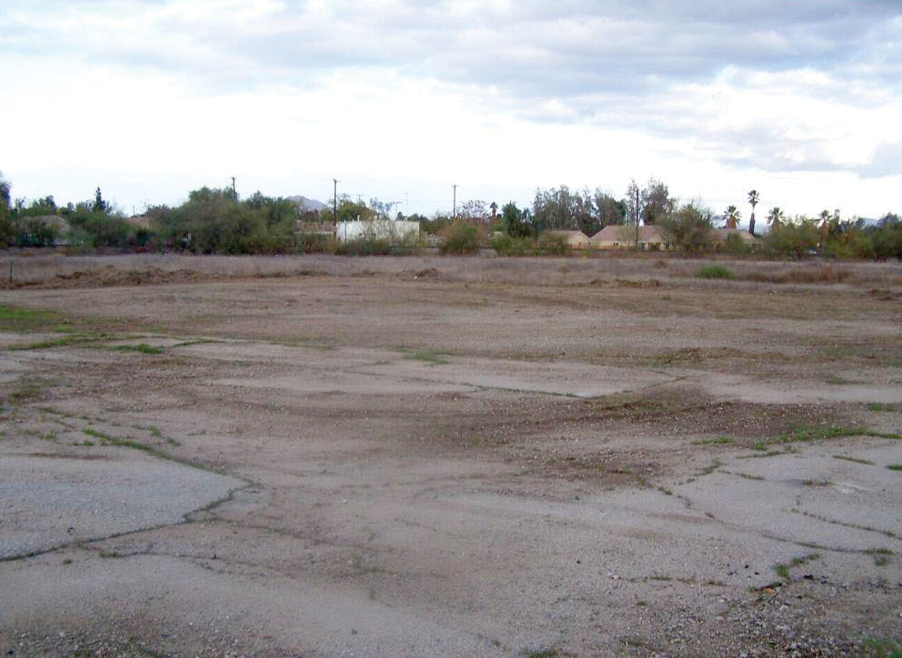 A vacant lot with some cracked pavement, dirt, and patches of grass