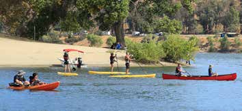 People paddling canoes kayaks, and stand up paddle boards on a lake near a beach